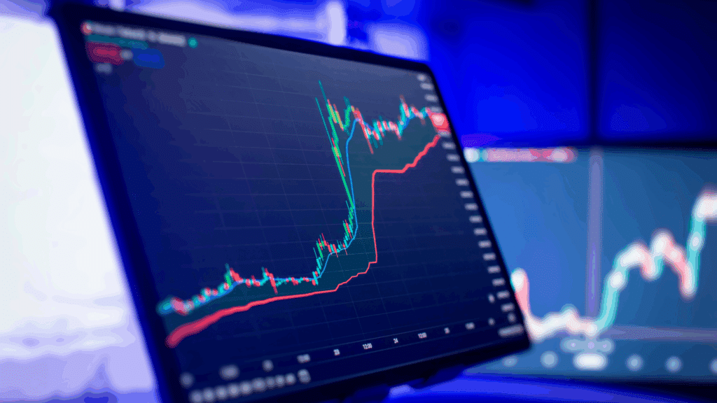 A close-up shot of a computer screen displaying a financial candlestick chart and line graphs, with a deep blue background. The chart shows a significant upward trend, representing stock market data.